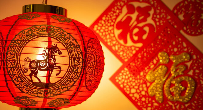 Close-up of red lantern with horse design, and red paper cut with golden characters, representing Chinese New Year celebration and culture