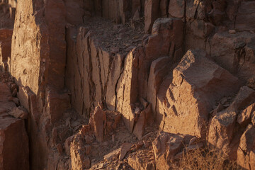 Rocky desert cliffs near Qom, Iran, illuminated by warm sunlight. The rugged brown formations show vertical fractures and natural textures, revealing the geological layers shaped by erosion.