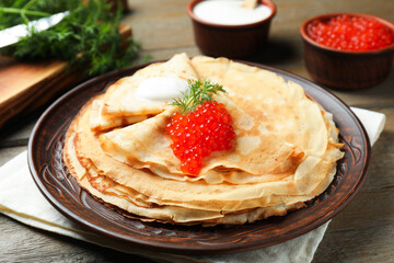 Tasty crepes with red caviar, sour cream and dill on wooden table, closeup
