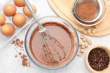 Chocolate dough with whisk in bowl, eggs and spices on grey textured table, flat lay