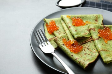 Tasty spinach crepes with red caviar and sour cream on grey table, closeup. Space for text