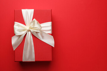 Beautiful gift with bow on red background, top view. Space for text