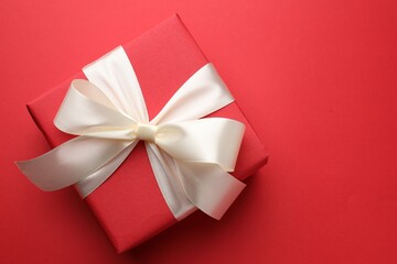 Beautiful gift with bow on red background, top view