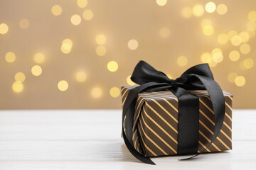Beautifully wrapped gift on white wooden table against blurred lights, closeup. Space for text