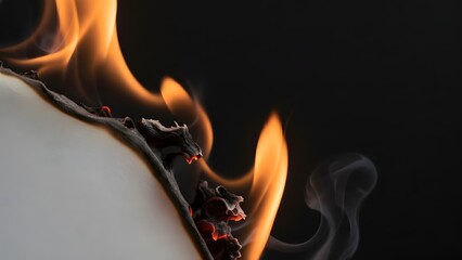 A closeup view of a burning object with flames and smoke on a dark background