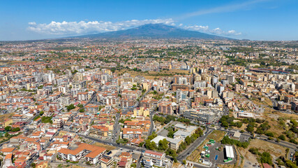 Fototapeta premium Aerial view at morning of the outskirts of Catania, Sicily, Italy. In the background, on the horizon, Mount Etna looms in silhouette, dominating the panorama.