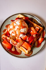 Overhead waffle dessert with vanilla ice cream, strawberries, and caramel sauce on a white background. Clean top-down composition ideal for menus, food branding, and editorial design.