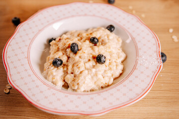 Creamy oatmeal porridge with blueberries in a ceramic bowl on a wooden table. Soft natural light and cozy atmosphere, ideal for healthy breakfast concepts