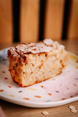 Close-up of a slice of homemade apple cake dusted with powdered sugar. Soft natural light and shallow depth of field create a warm, cozy café mood