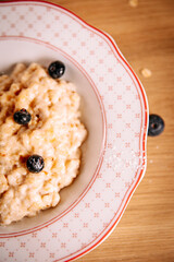 Close-up view of creamy oatmeal porridge topped with blueberries. Minimal and cozy healthy breakfast detail on a wooden table with natural light