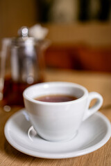 White cup of hot tea on saucer in cozy cafe interior. Minimal lifestyle scene with warm tones, soft focus and calm atmosphere.