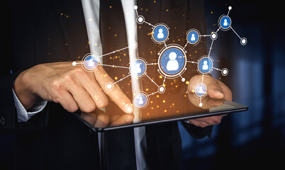 A businessman interacts with a digital tablet displaying a virtual network of people and communication icons, symbolizing modern connectivity and data interaction. Tessel