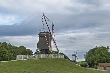 Windmill landscape in Bruges featuring a traditional wooden windmill with red and white blades on a...