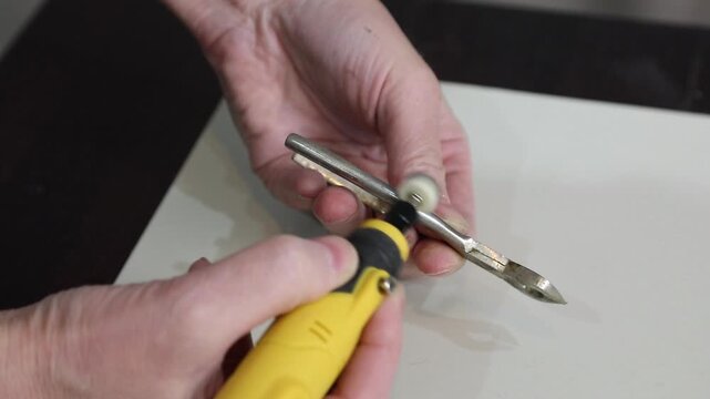 Woman using a handheld sander to restore vintage sugar tongs by removing patina and polishing the old metal utensil.