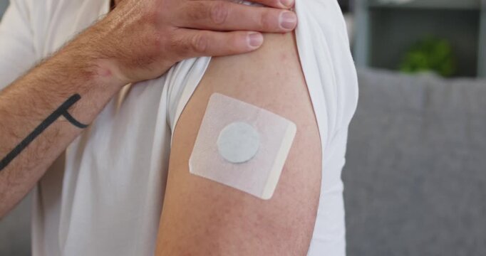 Man shows patch sensor for diabetes glucose. Wearable device on upper arm tracks levels, supporting health management and doctor-guided monitoring at home. Idea: home glucose monitor wearable.