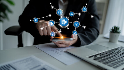 A focused businessman uses a smartphone while exploring digital icons representing management and strategy in a modern office setting, highlighting connectivity. Tessel