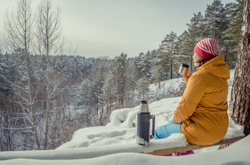 A girl drinks tea from a thermos in winter outdoors