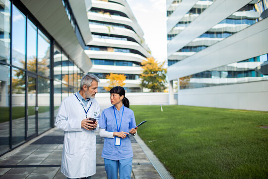 Mature doctor and adult nurse in serious discussion outside hospital