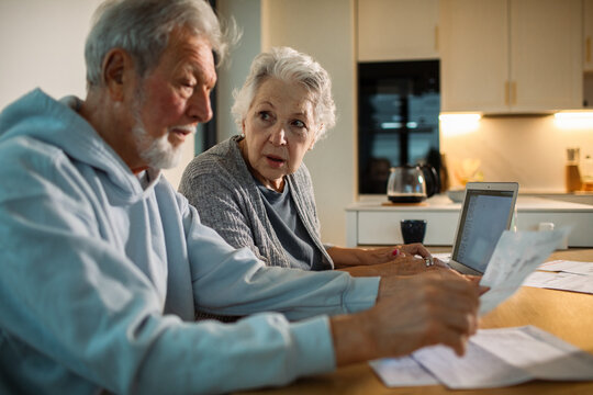 Senior couple worried reviewing bills at home kitchen