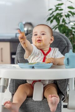 Messy baby holding spoon during self-feeding time. Complementary feeding