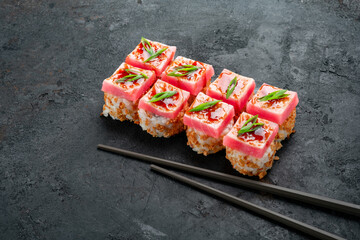 Elegant tuna sushi rolls topped with fresh raw tuna, teriyaki glaze, and green onions, served with chopsticks on dark slate. Luxury Japanese maki, gourmet tuna roll, premium seafood sushi.