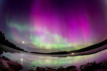 Broad arch of pink and green Aurora Borealis reflecting under a dark night sky at Kiser Lake, Ohio during the May 2024 solar storm (Fisheye landscape)