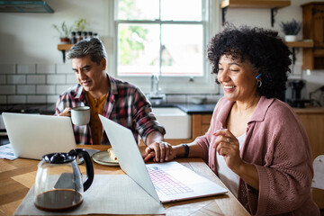 Mature adults working remotely and smiling in home kitchen