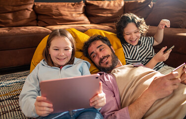 Adult father and children laughing using tablet in home living room