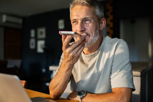 Mature man using smartphone voice assistant at home, focused