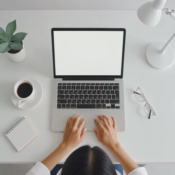 Overhead perspective of a contemporary office setup featuring an individual typing on a laptop, with a blank screen, suggesting focused work and digital tasks