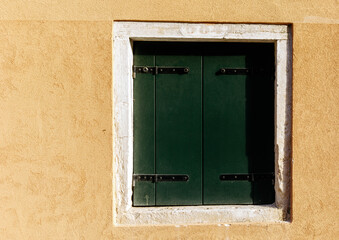 Closed green shutter on rustic beige wall with white frame