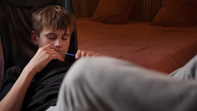 Pensive teenage boy sit in chair in bedroom, thoughtfully chewing on pen while contemplating solution, concentrating on difficult task or homework assignment