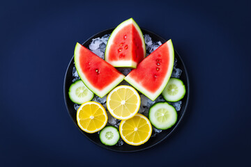 Watermelon, lemon slices and cucumber rounds arranged with ice on a dark plate, refreshing summer drink ingredients