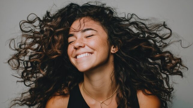Joyful young woman with curly hair expressing happiness and freedom with a confident smile and lively hair movement