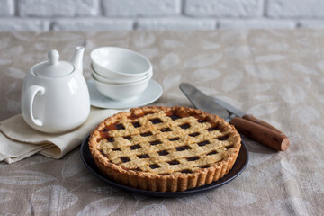 Freshly baked lattice pie on a rustic table beside stacked plates, bowls, and a white teapot, creating a cozy homemade dessert scene.