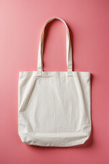 White empty tote bag laying on pink surface. Eco or reusable shopping bag. 