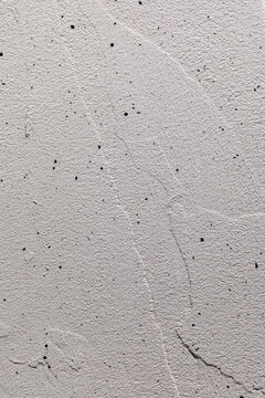 A white, haphazardly plastered wall is splattered with black paint. Vertical photo