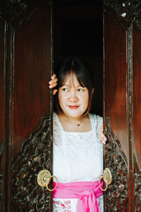 Balinese Woman Peeking Through Traditional Wooden Door in Cultural Setting