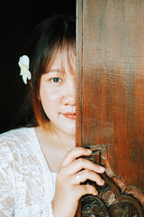 Balinese Woman Peeking from Behind Carved Traditional Wooden Door