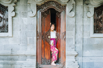 Balinese Woman Between Traditional Carved Wooden Doors