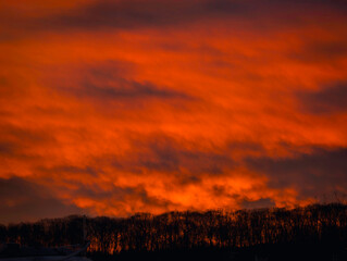 Sunrise with glowing orange clouds above the Quinnipiac River boat marina and forest hill in Fairhaven, New Haven County, Connecticut, United States, a radiant skyscape of light and natural beauty.