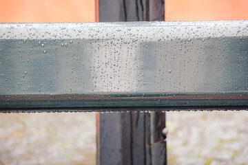 Close up of a smooth, grey metal railing covered in fresh rain drops with a blurred orange background