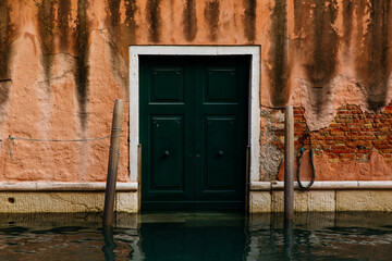 Venice, Italy - December 05, 2025: Green wooden door stands against a weathered pink wall, partially submerged in water, showcasing the unique architecture of Venice, Italy with historical charm
