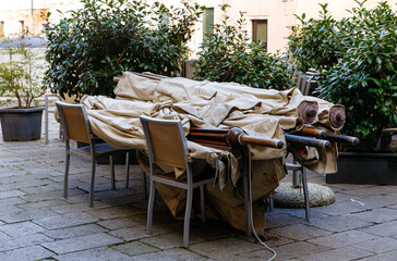 Venice, Italy - December 05, 2025: Outdoor dining area with stacked chairs and covered tables, showcasing a tranquil courtyard scene with lush greenery and urban architecture