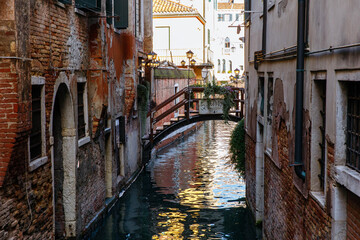 Venice, Italy - December 05, 2025: Scenic view of a narrow canal in Venice, Italy, featuring rustic brick buildings and a charming wooden bridge, capturing the essence of Venetian architecture