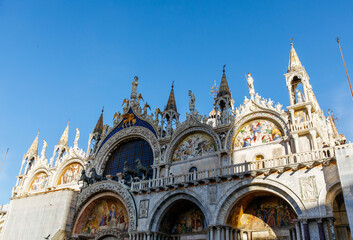 Naklejka premium Venice, Italy - December 05, 2025: St. Mark's Basilica in Venice showcases stunning architecture with intricate sculptures and vibrant mosaics under a clear blue sky, a symbol of historical beauty