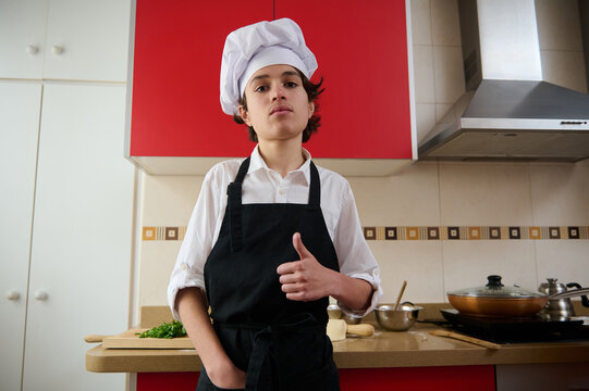 Young Chef In White Shirt And Black Apron Poses Confidently In Modern Kitchen