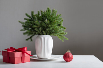 Creative Christmas tree alternative made from evergreen fir branches in ceramic vase with red gift box and ornament. Scandinavian style Xmas holiday decor.