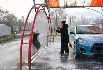 Woman cleaning car mat at a car wash on a chilly day in a city environment with residential