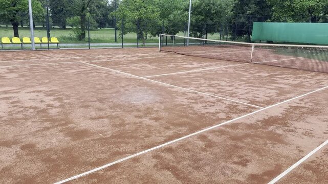 Wet clay tennis court with puddles during the rain. Outdoor tennis season. Spring rain on courts. All practices and match are cancelled